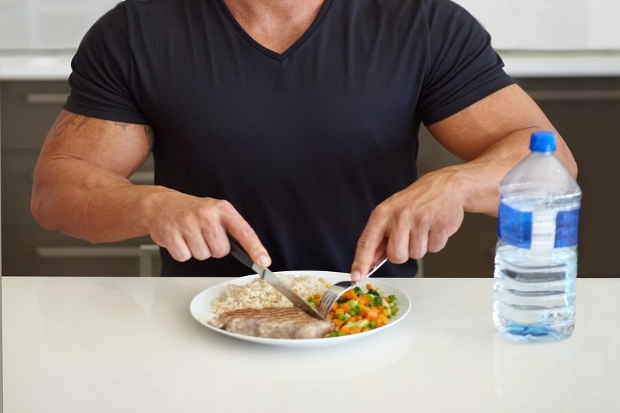 un bodybuilder qui mange équilibré avec une bouteille d'eau