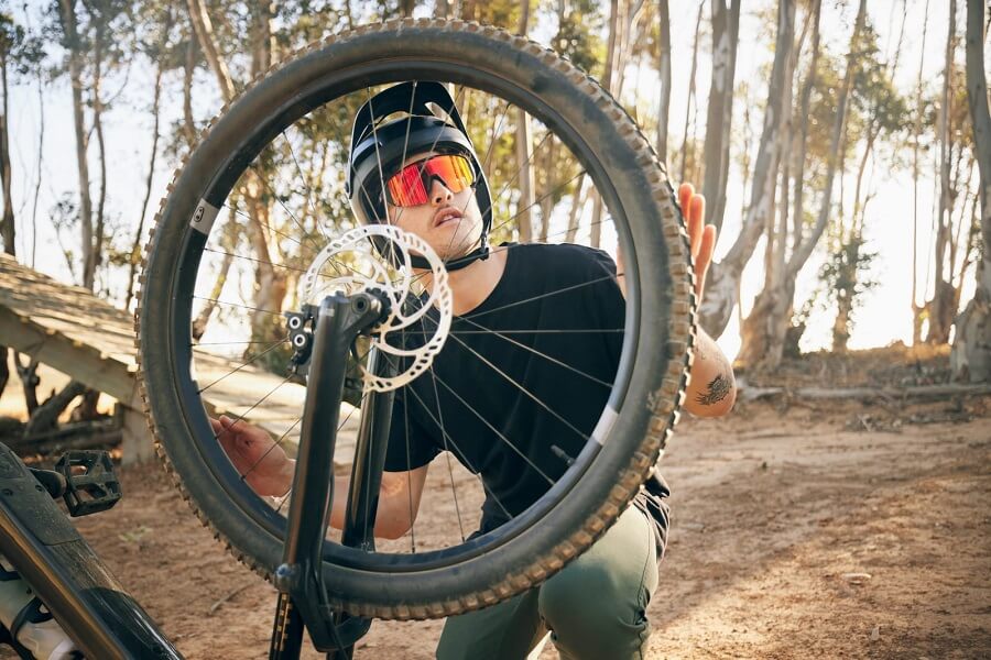 un cycliste qui inspecte ses pneus de bicyclette en forêt